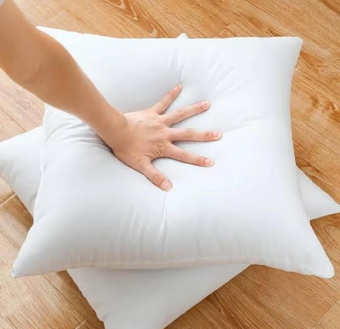 White pillow on a wooden floor with a hand pressing into it